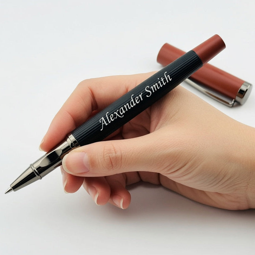 A hand holding a personalized black ballpoint pen with 'Alexander Smith' written in white script, with its brown cap placed behind it on a clean white background.