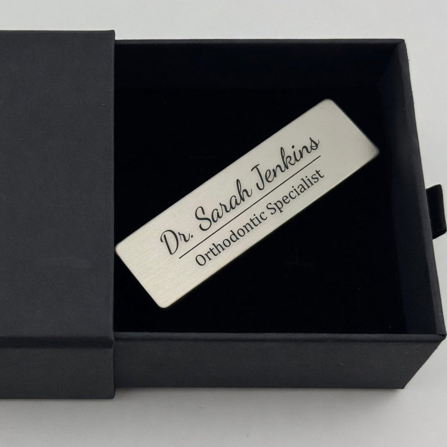 A personalized silver metal name plaque engraved with 'Dr. Sarah Jenkins Orthodontic Specialist', presented inside a black gift box.