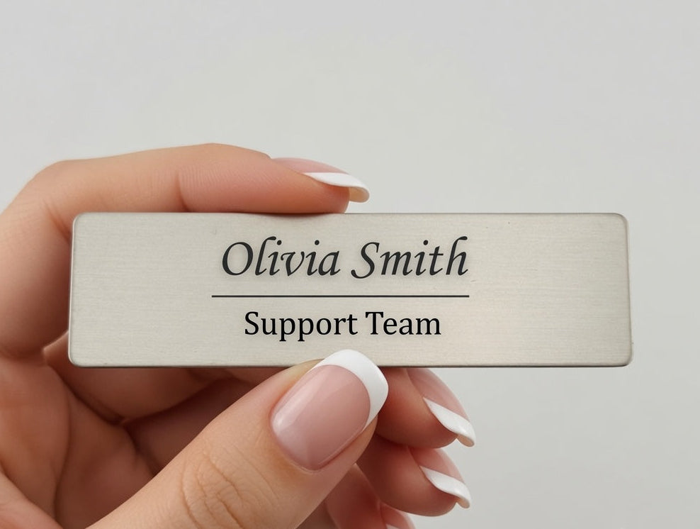 A hand with a French manicure holds a rectangular brushed-metal nameplate that reads 'Olivia Smith Support Team' against a light gray background, with 'Style 2' text in the lower right corner.