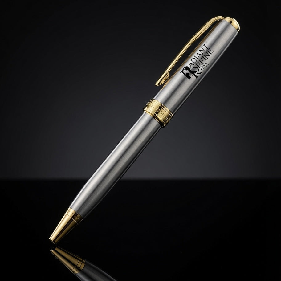 A metallic silver ballpoint pen with gold trim and a black printed logo, shown diagonally on a reflective black surface against a dark gradient background.