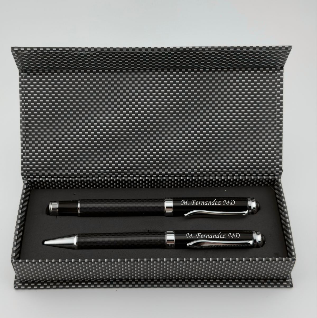 A black pen and ballpoint pen gift set in an open textured black presentation box, photographed on a light gray background.