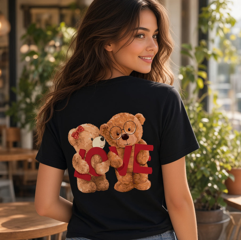 A woman wearing a black t-shirt with a graphic of two teddy bears hugging and the word 'LOVE' in red, photographed in a bright, modern cafe setting.