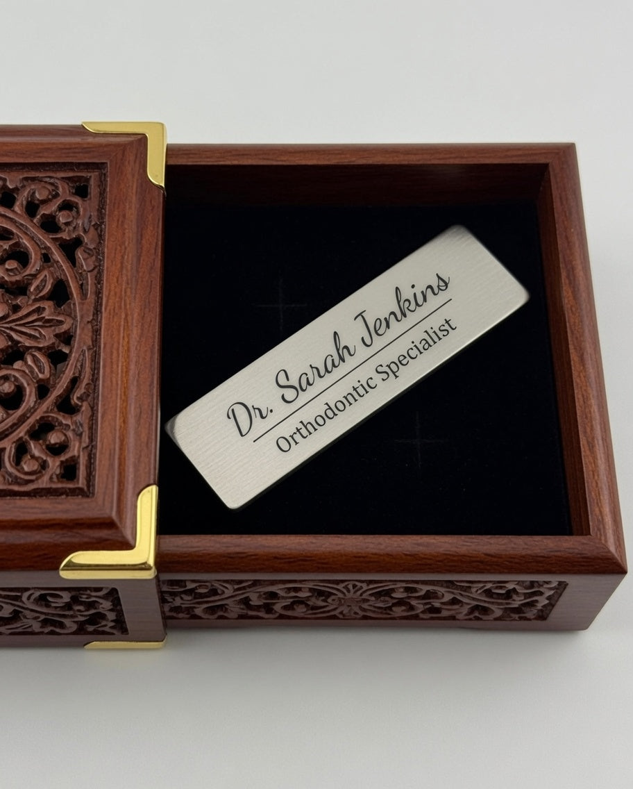 A personalized silver metal plaque engraved with 'Dr. Sarah Jenkins Orthodontic Specialist' resting inside an open dark brown carved wooden keepsake box with gold corner accents.