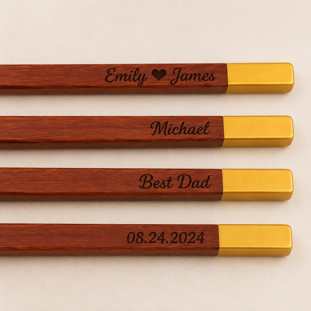 Four wooden chopsticks with gold metal tips, each engraved with a personalized name or date, arranged horizontally on a light beige background.