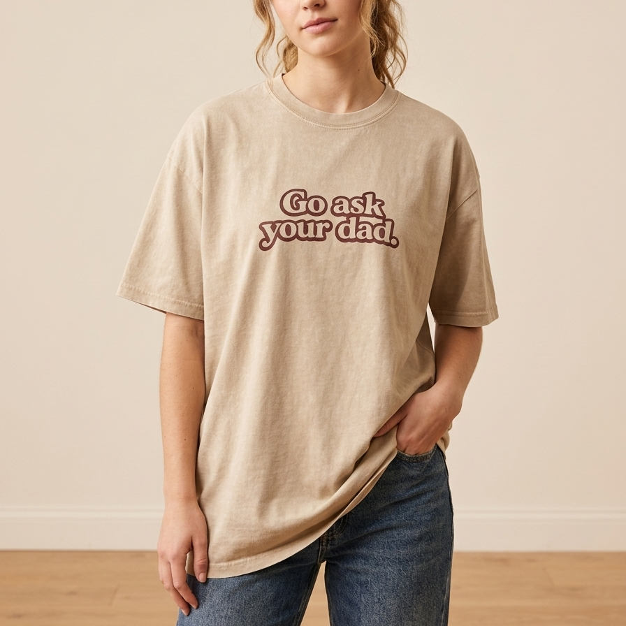 Person wearing a beige t-shirt with text, standing against a plain background