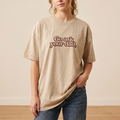 Person wearing a beige t-shirt with text, standing against a plain background