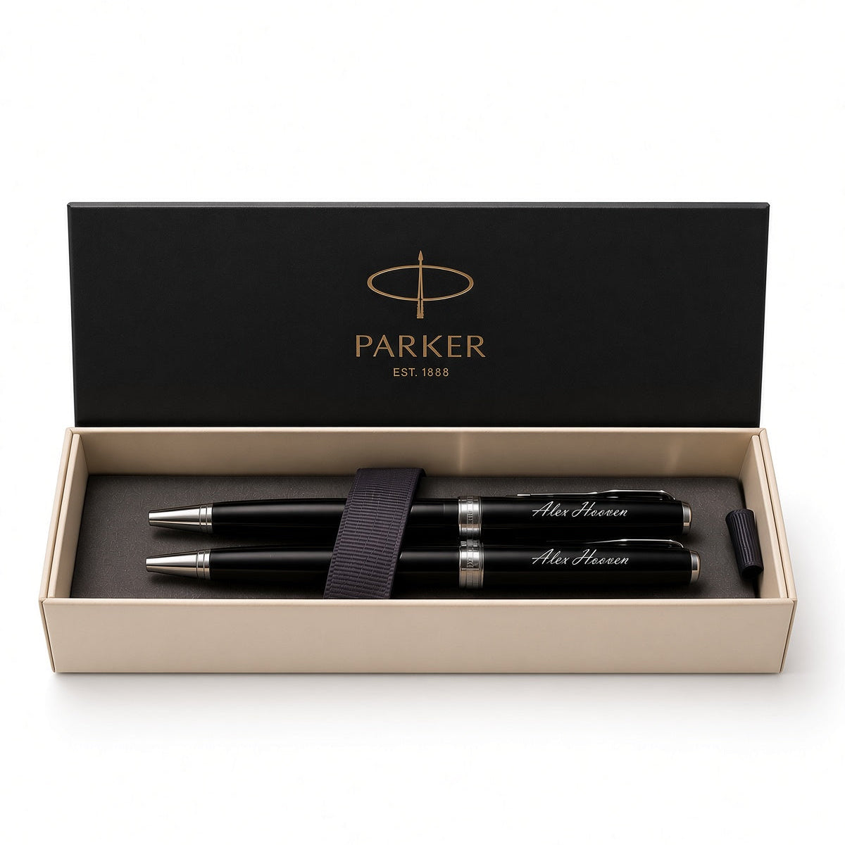 A Parker pen set in an open presentation box. The set includes two black pens with silver trim and white script engraving, a black elastic band, and a black cap, all inside a beige box with a black lid printed with the gold Parker logo.