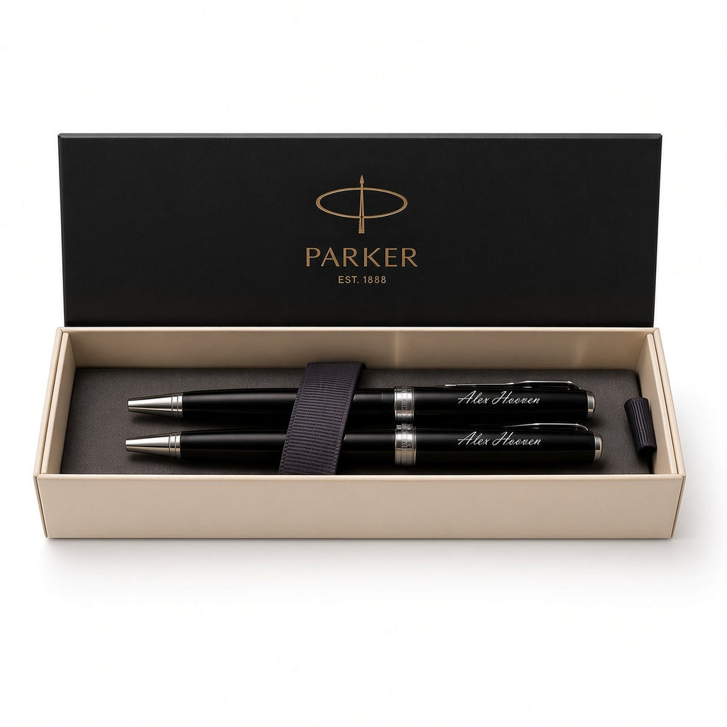 A Parker pen set in an open presentation box. The set includes two black pens with silver trim and white script engraving, a black elastic band, and a black cap, all inside a beige box with a black lid printed with the gold Parker logo.