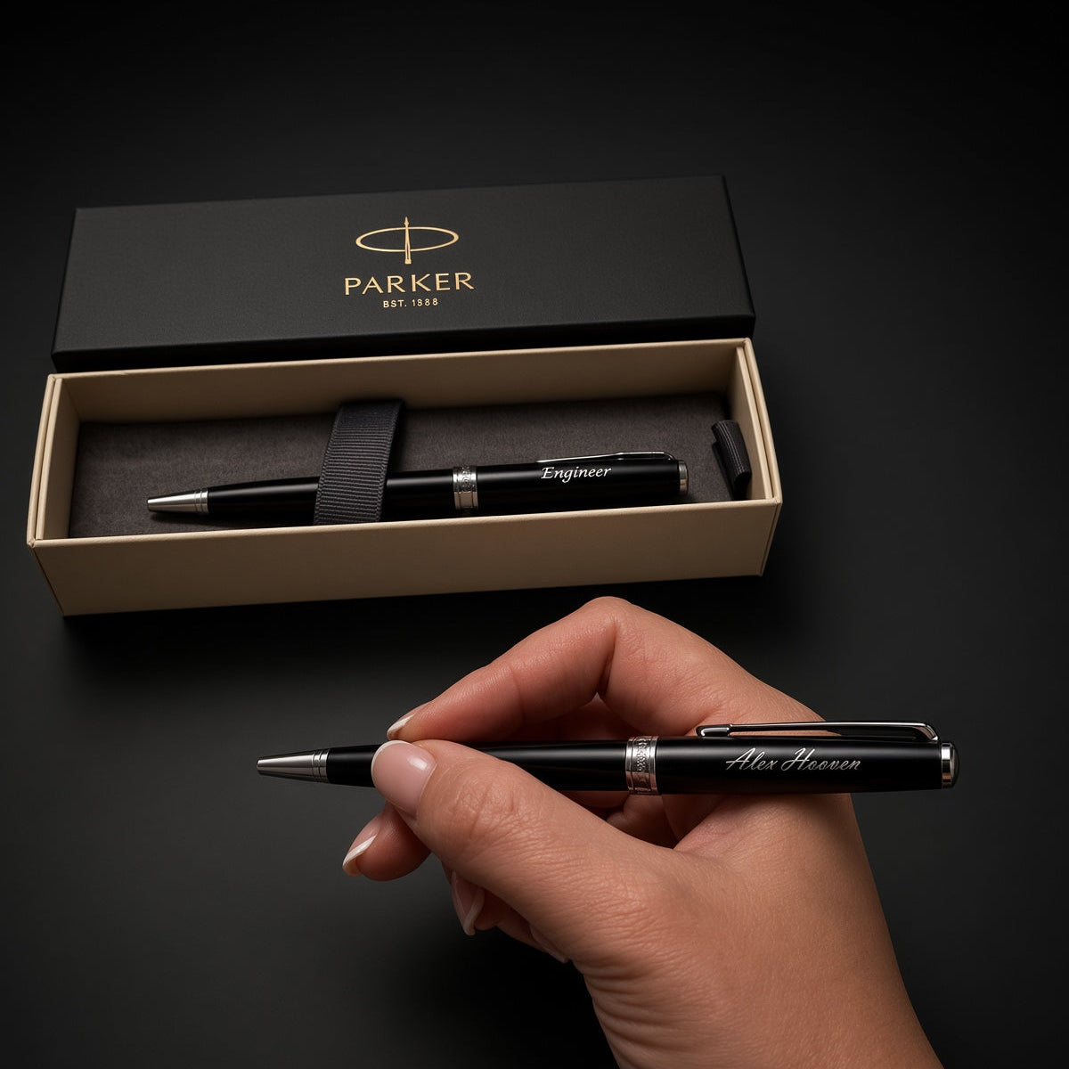 A hand holds a black Parker Signatur fountain pen with silver trim, with its open presentation box in the background on a dark surface.