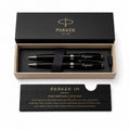 Parker IM pen set in a black presentation box with a matching black card, photographed on a clean white background. The set includes two black pens with silver and gold accents, a black ribbon, and branded packaging.