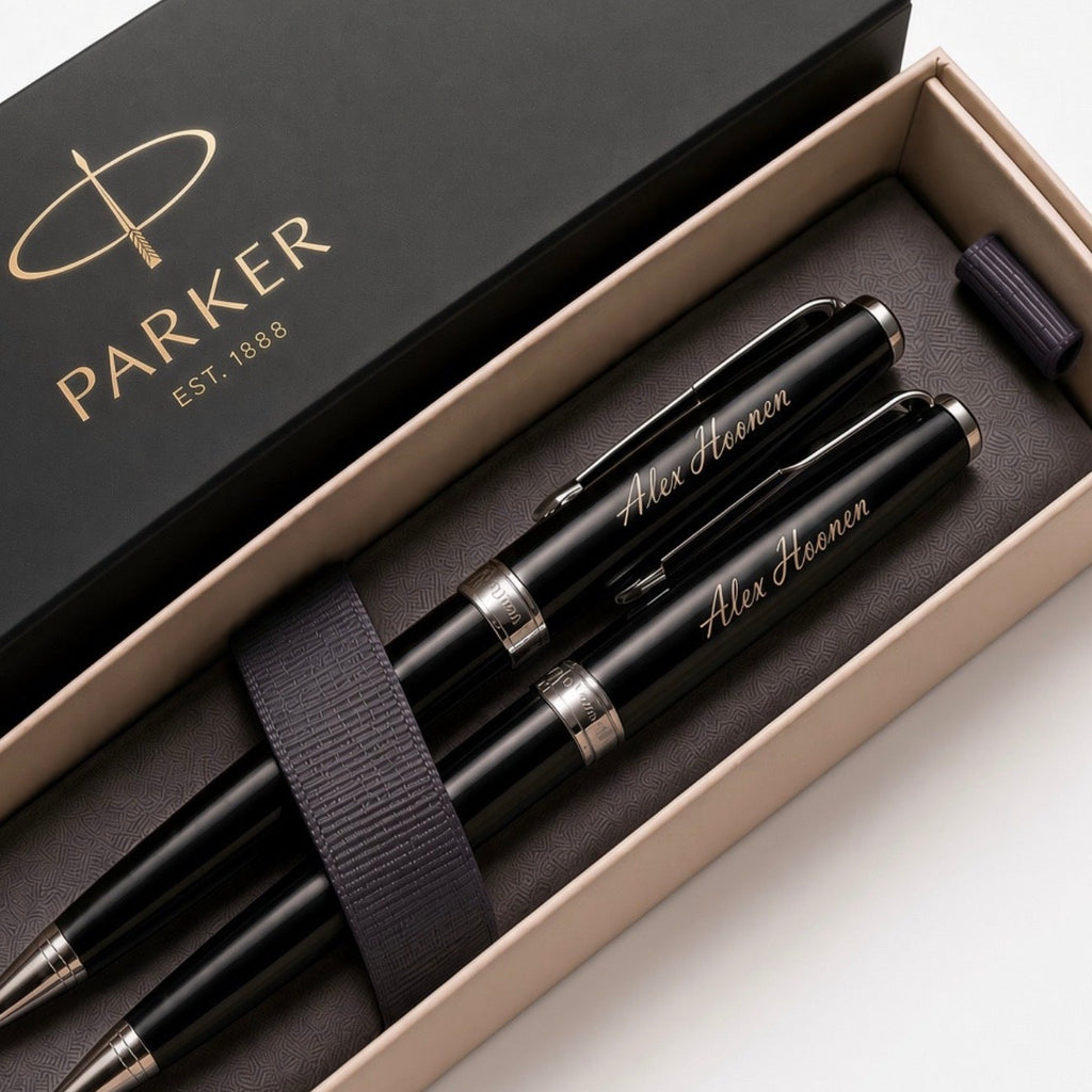 A Parker pen and ballpoint set in an open presentation box with the branded black lid visible. The set includes three black pens with silver trim and gold script personalization, plus a dark elastic band, photographed on a clean white background.