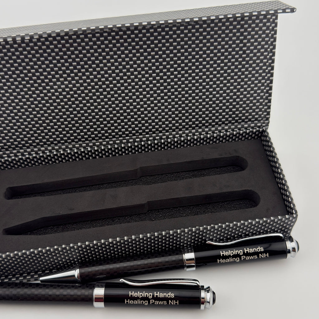 A black and silver pen and pencil set with custom white text reading 'Helping Hands Healing Power #4', displayed in front of an open textured black and silver presentation box on a light gray background.