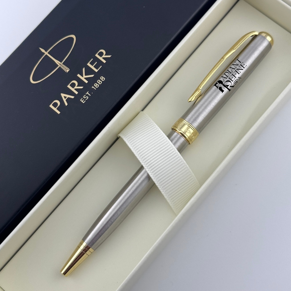 A Parker ballpoint pen with a silver body and gold accents, presented inside an open cream-colored gift box next to its dark navy blue lid, which features the gold 'PARKER EST. 1888' logo.