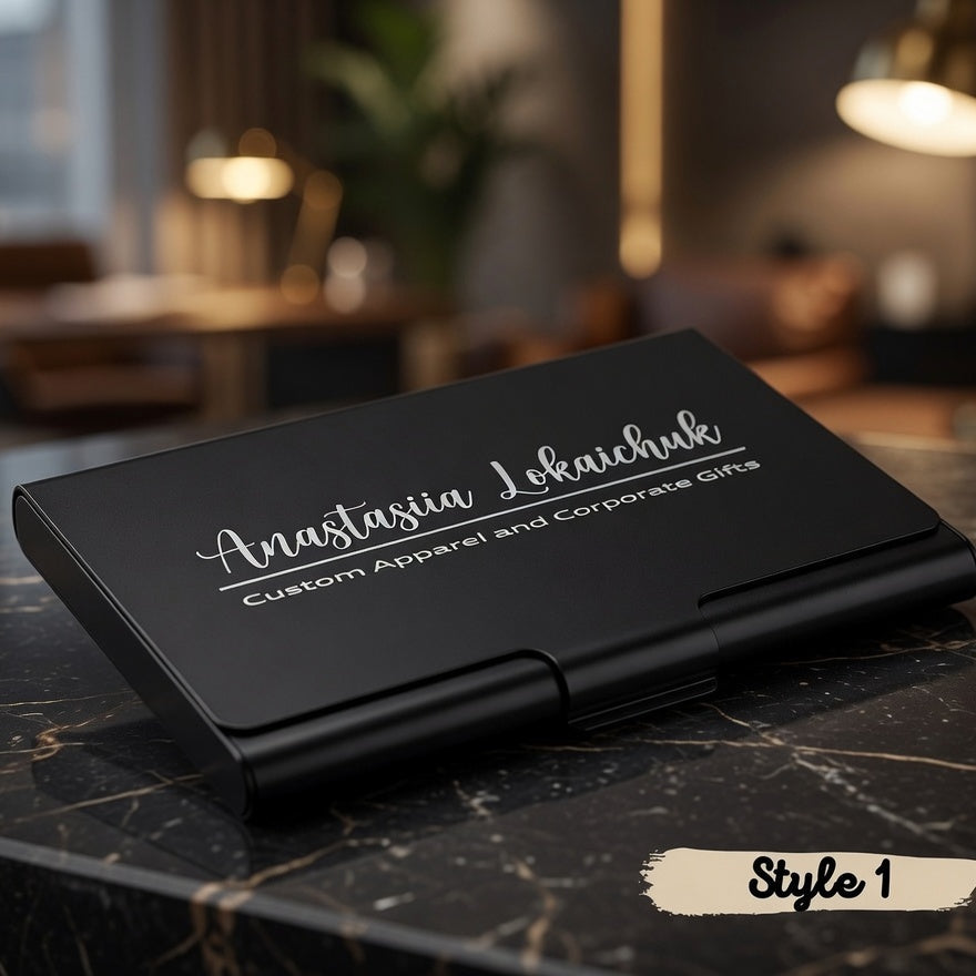 A black rectangular hard case with custom white script text reading 'Anastasia Lokachev' and smaller text 'Custom Apparel and Corporate Gifts' sits on a dark marble tabletop in a softly blurred indoor setting. A small 'Style 1' label appears in the lower right corner.