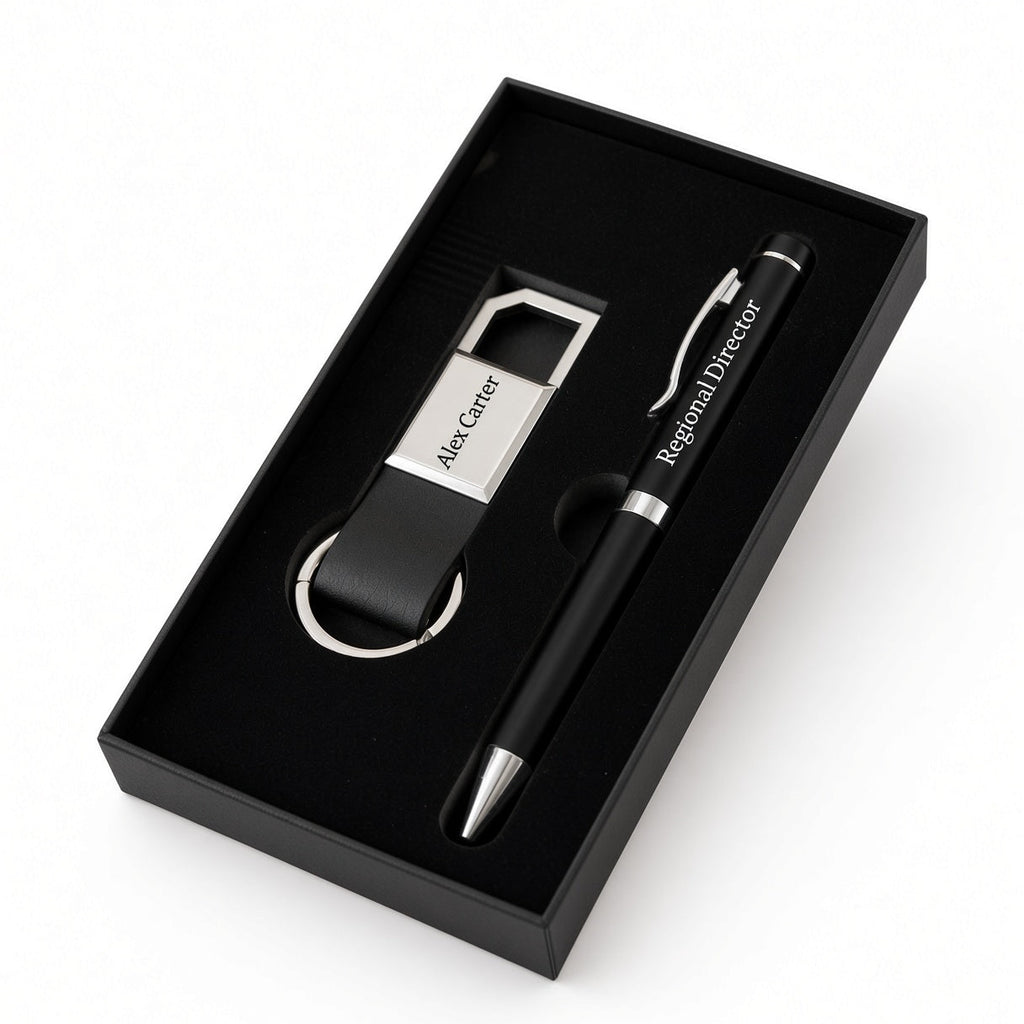 A black and silver personalized gift set inside a black presentation box, featuring a pen engraved with 'Regional Director' and a keychain with a silver metal tag engraved with 'Alex Carter'.