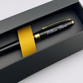 A personalized black ballpoint pen with gold trim and clip, featuring the name 'William Davis' in white script, presented inside a black gift box with a gold ribbon.