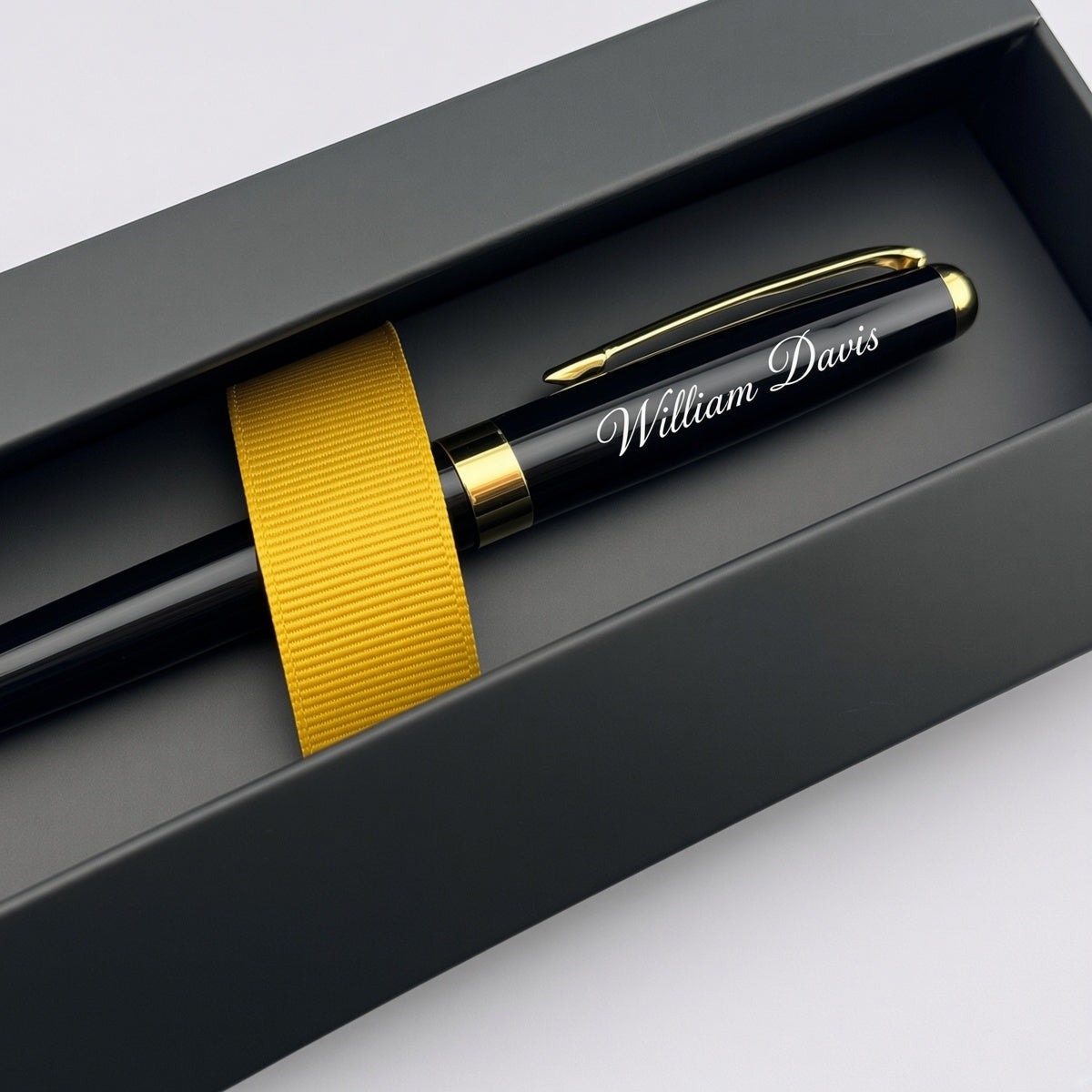 A personalized black ballpoint pen with gold trim and clip, featuring the name 'William Davis' in white script, presented inside a black gift box with a gold ribbon.